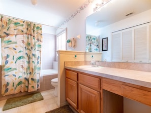 A bathroom with a shower curtain, toilet, sink, wooden cabinets, and a mirror.