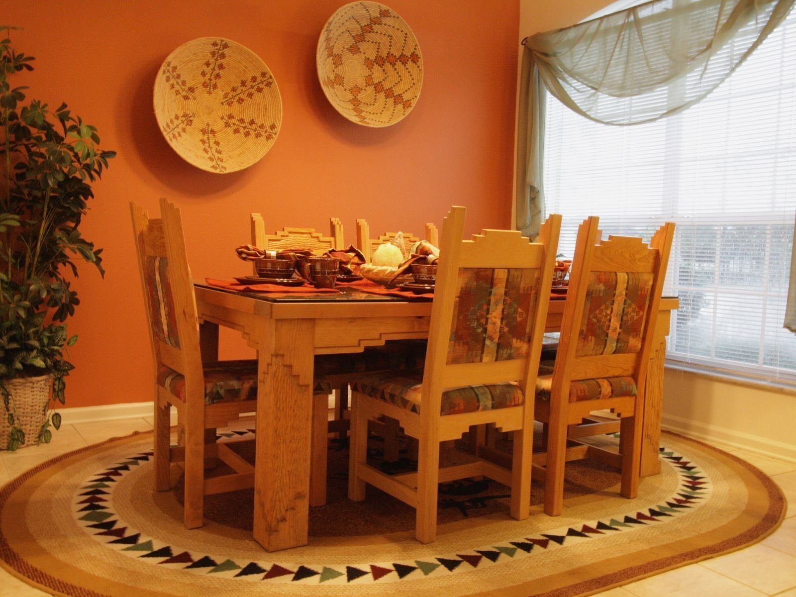A dining area with a wooden table and chairs, surrounded by a patterned rug.