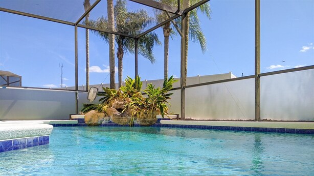 A clear pool with a rock feature and palm trees in the background. - 5 Bed 8002 (Kissimmee)