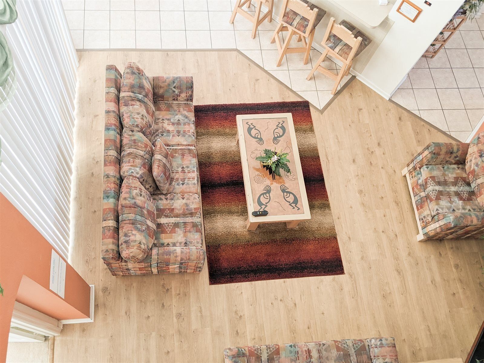 Une pièce aux hauts plafonds, avec un canapé d’angle, une petite table basse agrémentée d’un arrangement floral et un tapis à motifs.