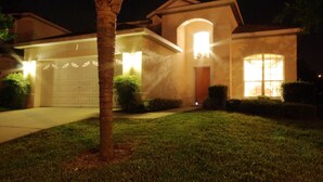 A residential house at night with a well-lit garage, a large window, and a lawn. - 5 Bed 8002 (Kissimmee)