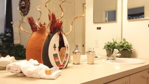 A bathroom with a beige countertop, a large mirror, a sink, a decorative vase, and a potted plant. - 5 Bed 8002 (Kissimmee)