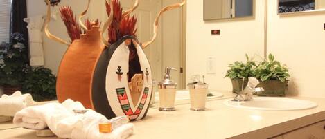A bathroom with a beige countertop, a large mirror, a sink, a decorative vase, and a potted plant.