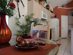 A kitchen with white cabinets, a microwave, and a refrigerator. There are plants on the counter and a vase with flowers.