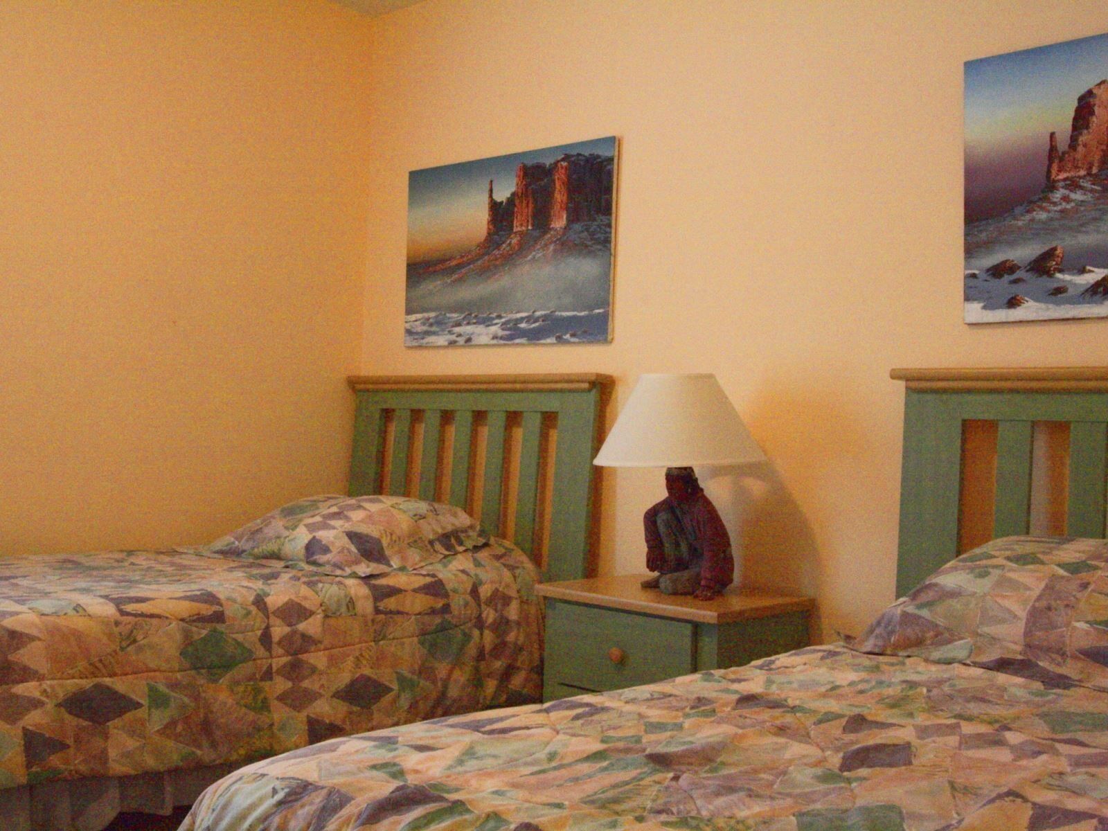 Quarto com duas camas, cada uma com colcha estampada. Um criado-mudo com abajur fica entre as camas.