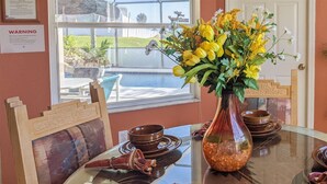 A dining table with a glass top, surrounded by wooden chairs, and a vase with yellow flowers. - 5 Bed 8002 (Kissimmee)