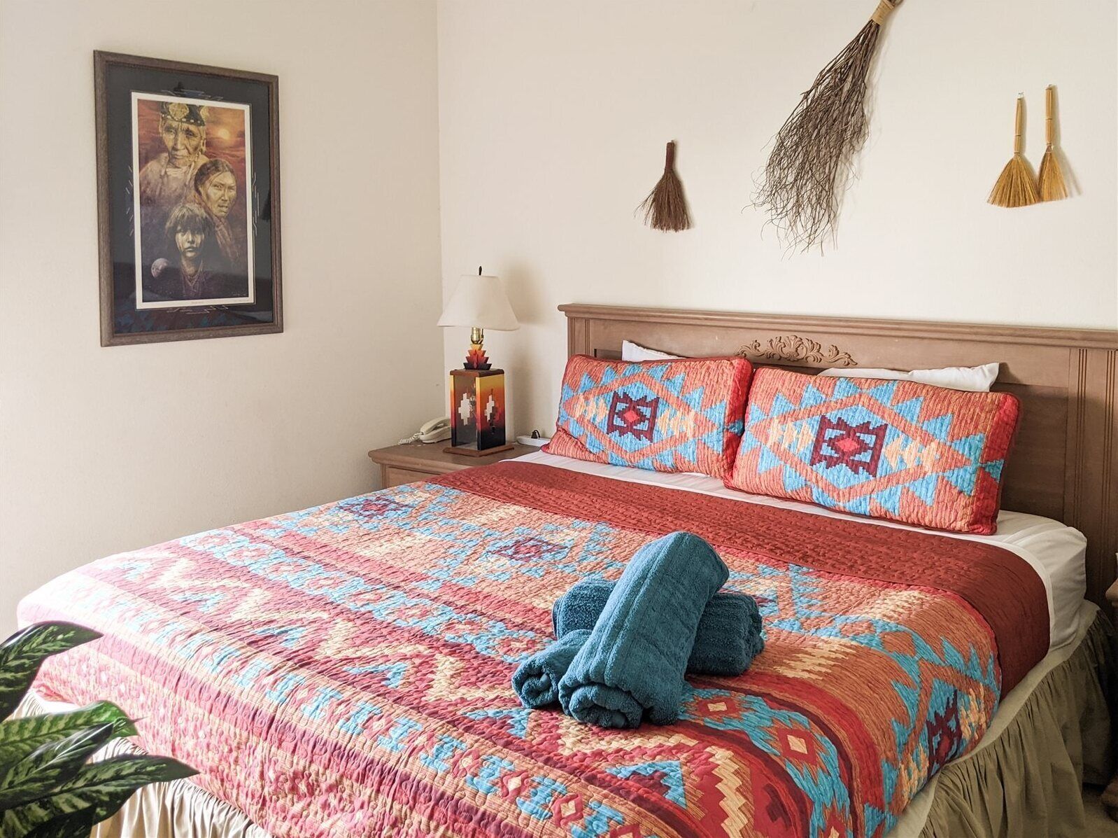 A neatly made bed with a patterned bedspread, two pillows with geometric designs, a bedside lamp, and a framed picture on the wall.