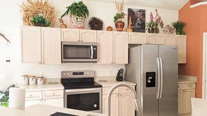 A modern kitchen with stainless steel appliances, light wood cabinets, and decorative plants. - 5 Bed 8002 (Kissimmee)