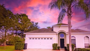A single-story house with a garage, a circular window above the door, and a palm tree in the front yard. - 4 Bed 2269 (Kissimmee)