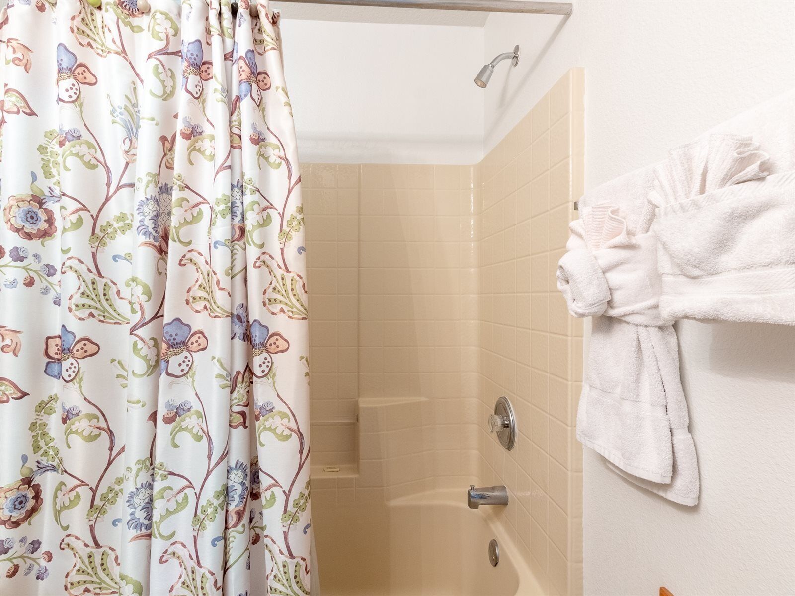 A bathroom with a shower, beige tiles, a floral shower curtain, and a towel rack with a white towel.