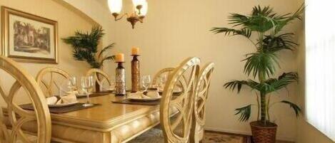 Comedor con mesa de madera, sillas, una lámpara de araña y plantas en macetas.
