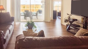 A living room with a sofa, a coffee table with a plant, a television, and a dining area with chairs and a table. - 4 Bed 428 (Davenport)