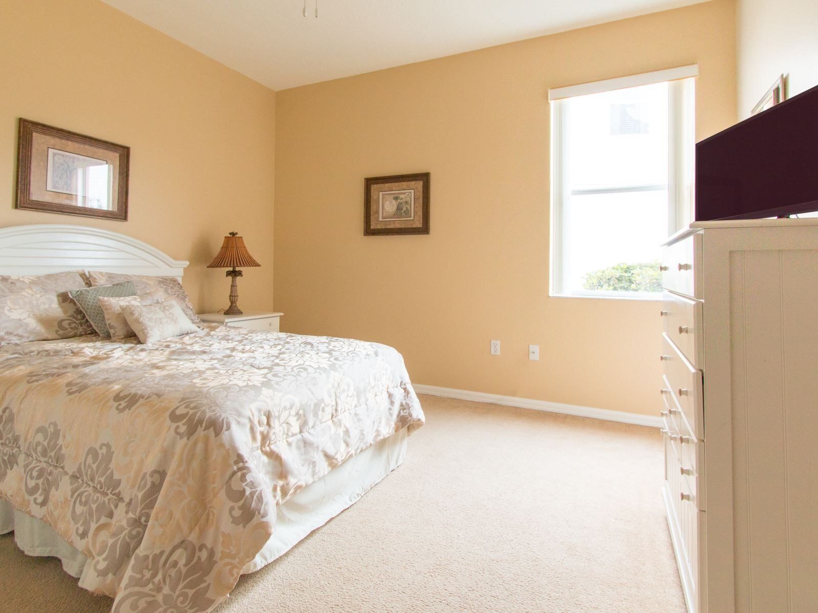 A bedroom with a bed, nightstand, lamp, dresser, and two framed pictures on the wall.