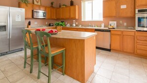 A kitchen with wooden cabinets, a stainless steel refrigerator, a microwave, a sink, and a large island with chairs. - 5 Bed 388 (Davenport)