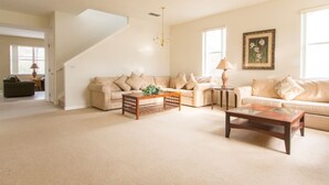 A spacious living room with a high ceiling, a staircase, and a large window providing natural light. - 5 Bed 388 (Davenport)
