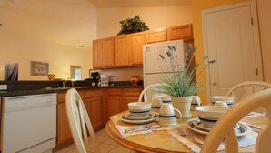 A compact kitchen with wooden cabinets, a refrigerator, and a dining table set for four. - 4 Bed 231 (Davenport)
