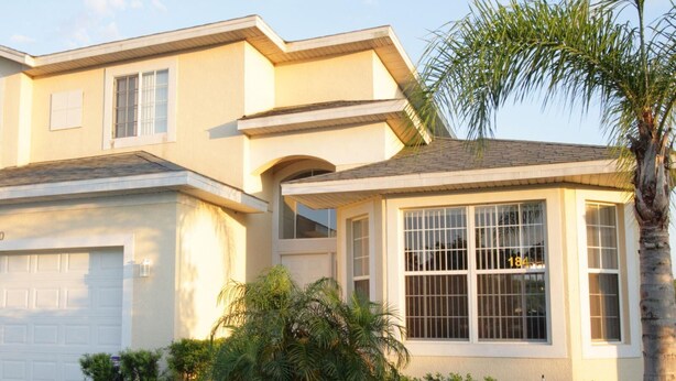 A two-story house with a garage, large windows, and a well-maintained garden with palm trees and shrubs. - 5 Bed 4720 (Kissimmee)