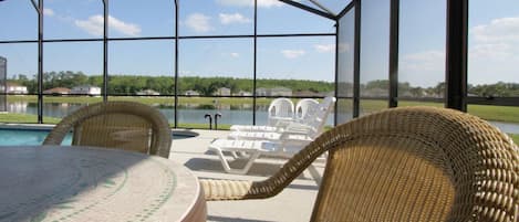A covered outdoor area with a pool, wicker chairs, and a view of a lake and buildings.