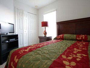 A bedroom with a bed, a television on a stand, a lamp, and a window.