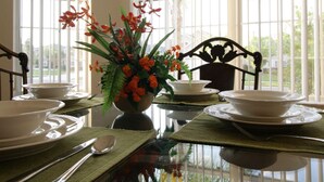 A dining table set with plates, bowls, and a vase of flowers, positioned near a window with a view of greenery. - 5 Bed 4720 (Kissimmee)
