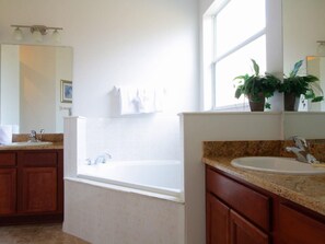 A modern bathroom with a bathtub, a sink, and a large mirror. There is a window providing natural light and a potted plant on the windowsill.