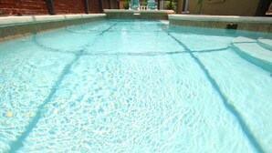 Una piscina cristalina con borde de azulejos y un muro de ladrillo al fondo.