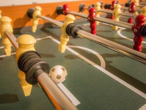Ein Detailbild eines Kickerapparats mit gelben und roten Spielfiguren, einem Fußball und einer grünen Spielfläche.
