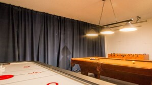 Una mesa de shuffleboard con una mesa de billar adyacente, una mesa de billar y un candelabro en el techo.