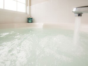 Eine Badewanne mit fließendem Wasser, ein Fenster und ein kleiner Behälter auf dem Boden.