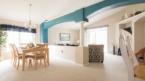 Amplia sala de estar con una mesa de comedor, sillas, un sillón estampado y una escalera.