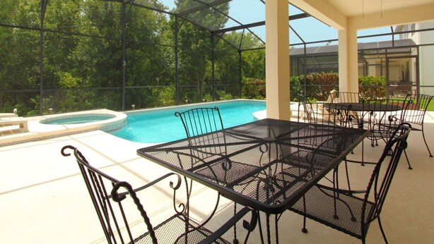 An outdoor pool area with a glass enclosure, surrounded by metal tables and chairs. - 6 Bed 2525 (Kissimmee)
