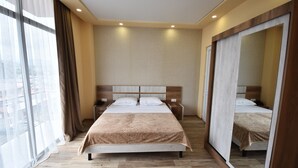 Een hotelkamer met een groot bed, nachtkastjes, een spiegel en uitzicht door het raam.
