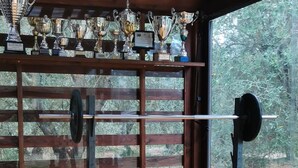 Une salle de sport équipée d’un banc de musculation, d’un support à squats et d’un mur où sont exposés des trophées.