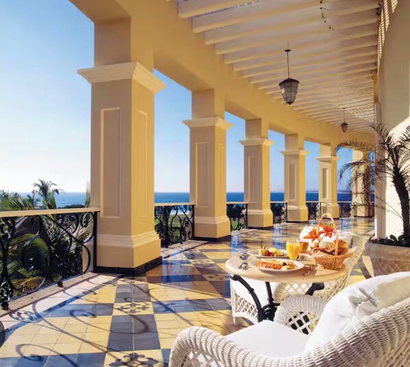 A terrace with a checkered floor, white wicker furniture, and a table set with breakfast.