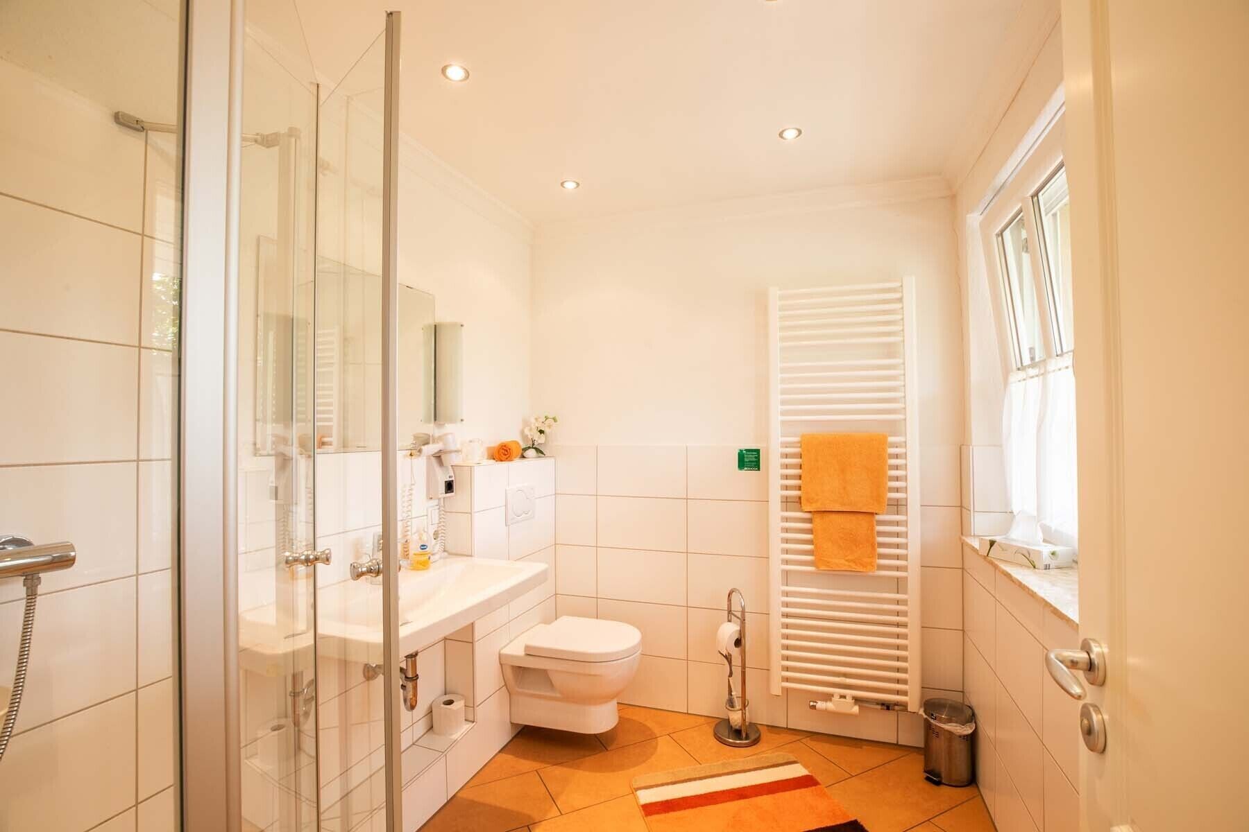A modern bathroom with a glass shower enclosure, a white sink, a toilet, and a towel rack with towels.