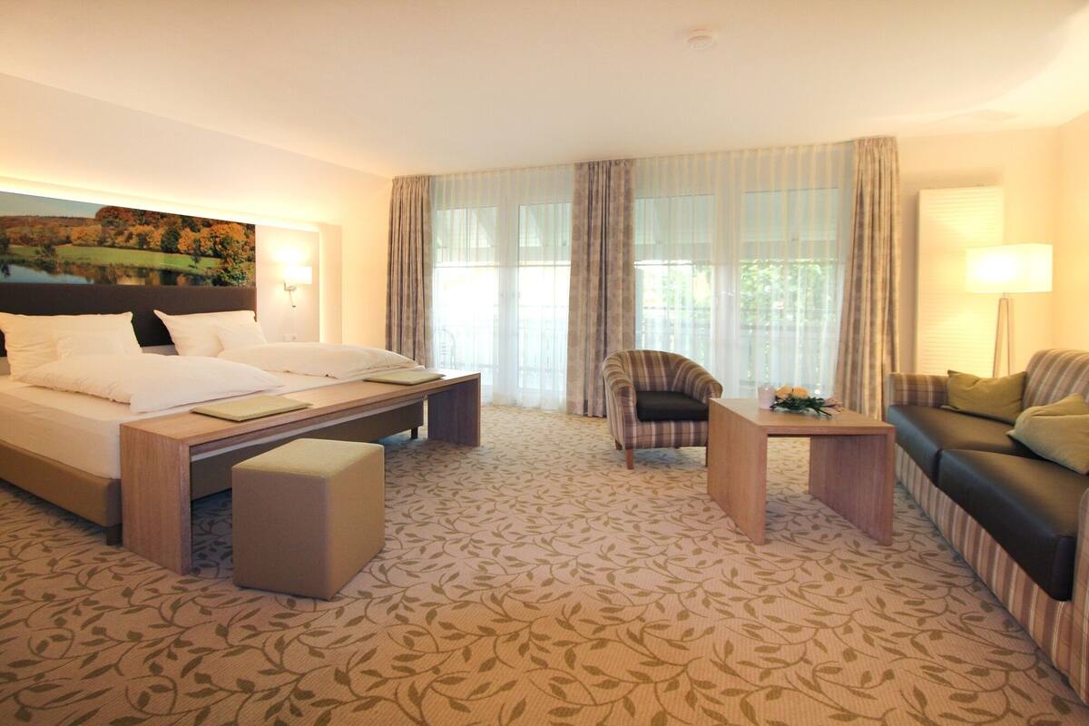 A hotel room with a bed, a chair, a sofa, a small table, and a painting on the wall.