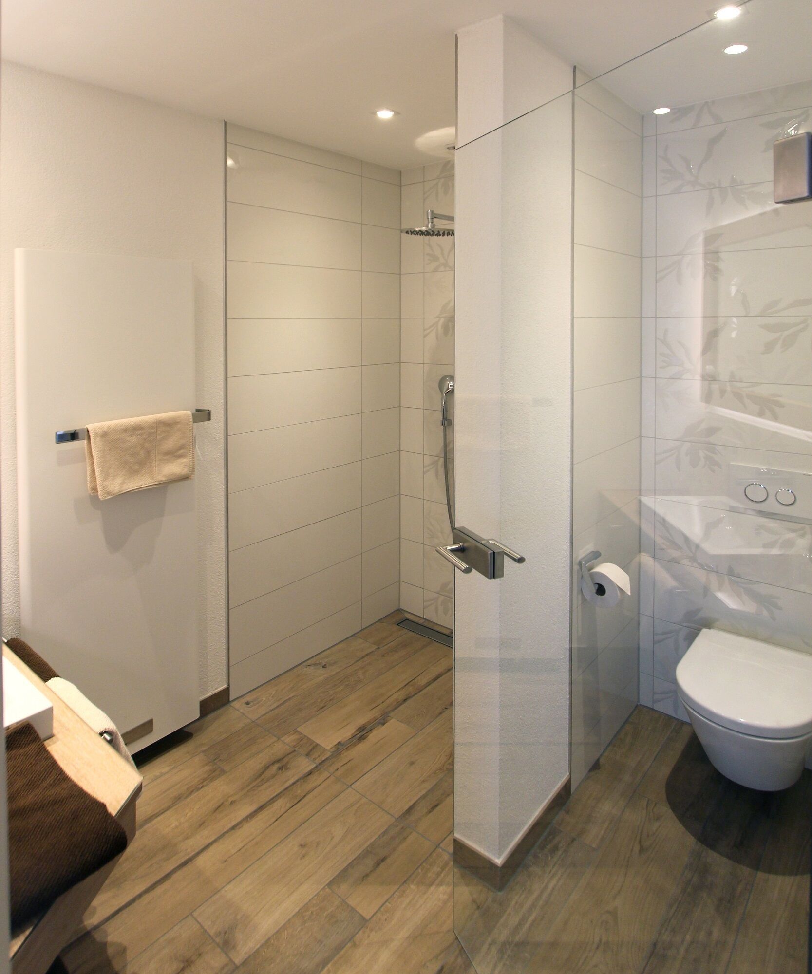 Un baño moderno con cabina de ducha de vidrio, inodoro y suelo de madera.