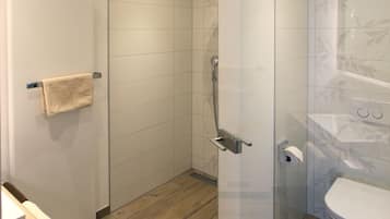 Un baño moderno con cabina de ducha de vidrio, inodoro y suelo de madera.