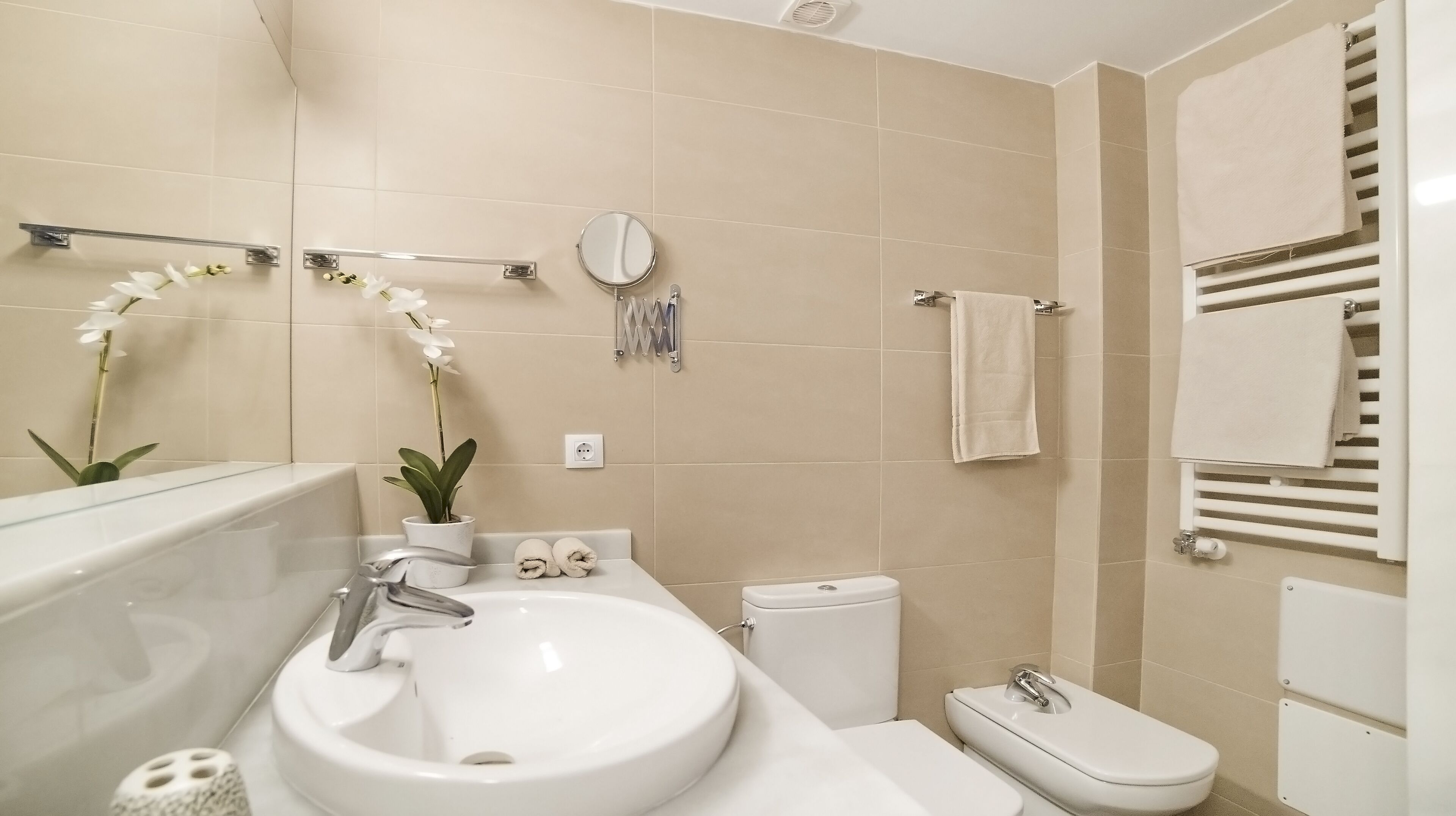 Un baño moderno con un lavabo blanco, inodoro y perchero para toallas.