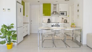 A modern kitchen with white cabinets, a green accent wall, a stainless steel range hood, a microwave, and a coffee maker. There are three clear stools at the island.