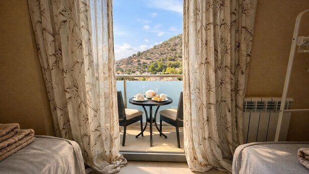 A balcony with a table set for tea, two chairs, and a view of a hilly landscape.