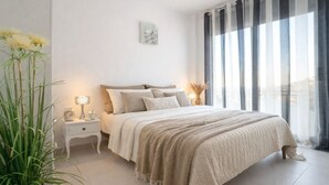 A modern bedroom with a large bed, bedside tables, and a view of the city through sheer curtains.