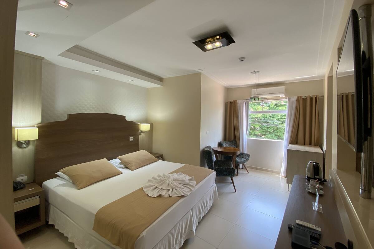 Habitación de hotel con una cama grande, un escritorio con silla, una ventana con cortinas e iluminación en el techo.