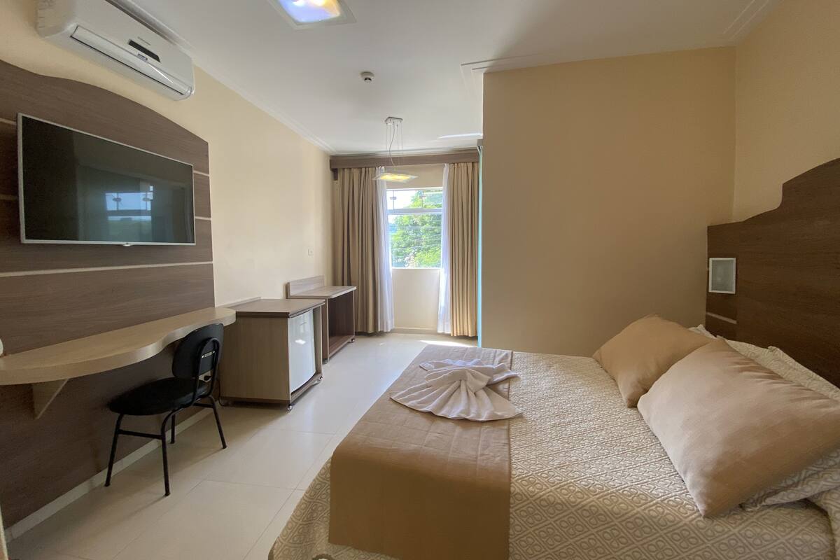 Una habitación de hotel con cama, escritorio, silla, televisor y ventana con cortinas.