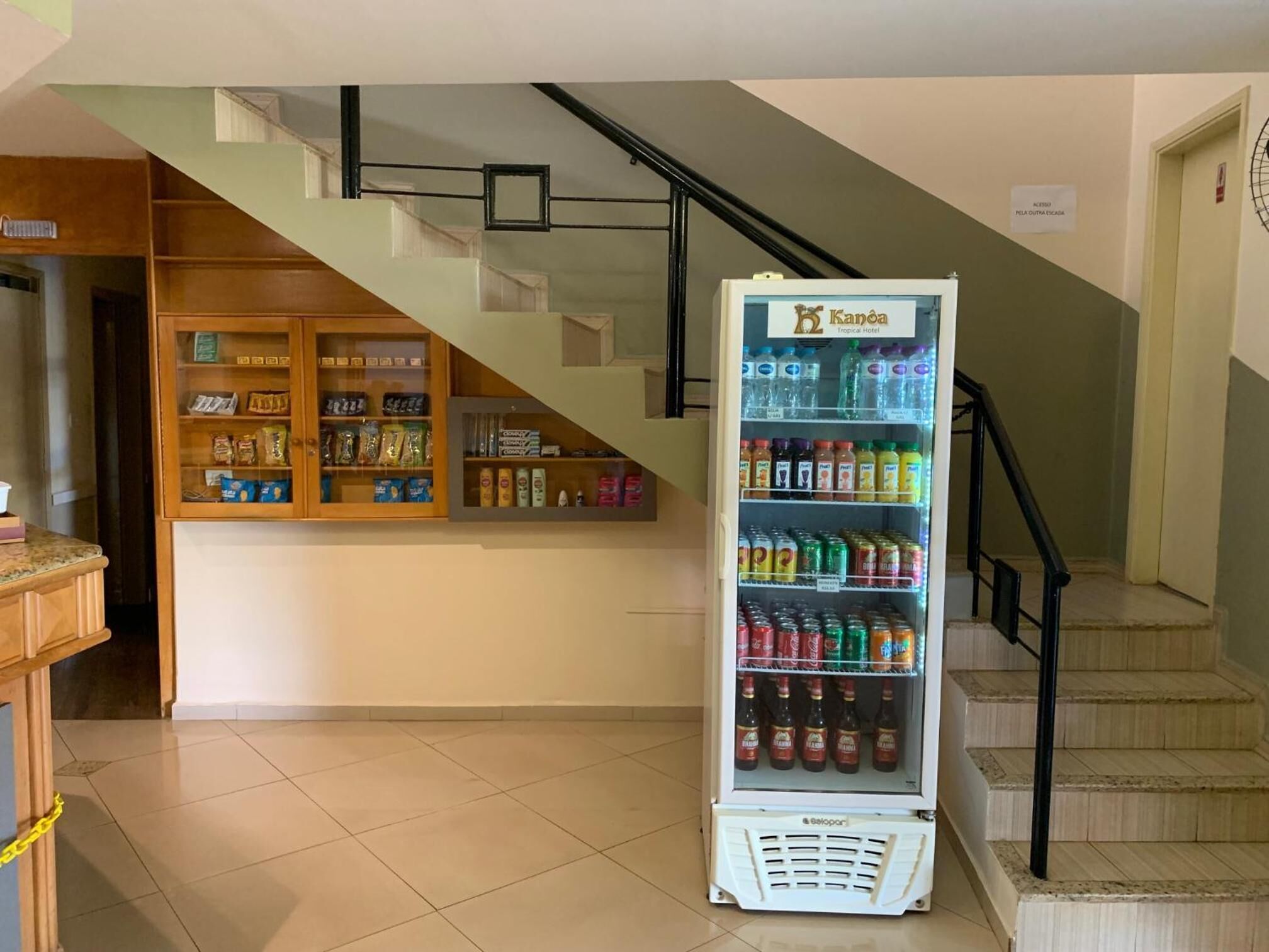 Un hall de hotel con una máquina expendedora llena de bebidas, una exhibición de aperitivos y una escalera.
