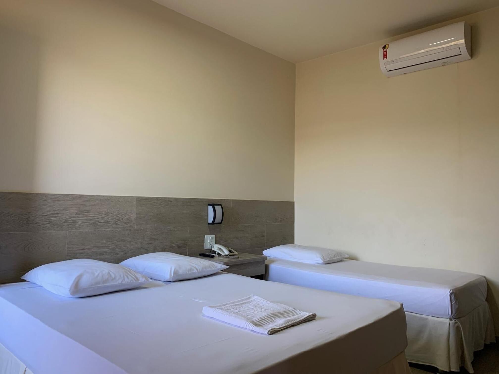 Habitación de hotel con dos camas, una mesita de noche con teléfono y un equipo de aire acondicionado en la pared.