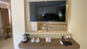 A hotel room with a large mirror, a coffee maker, two cups of coffee, a remote control, and a phone charging on a wooden table. - Kanoa Hotel (Santo Antônio da Platina)