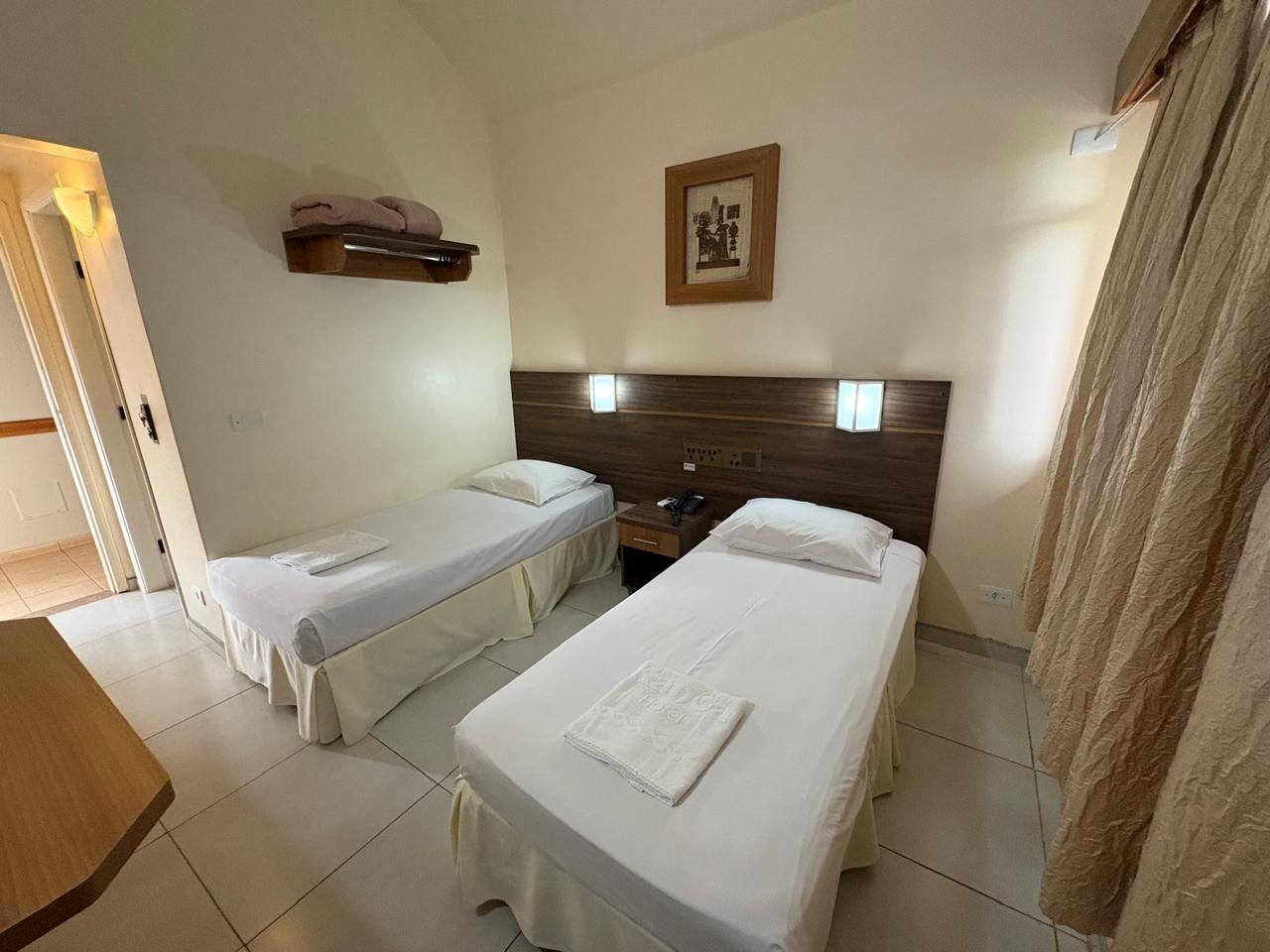 Een hotelkamer met twee enkele bedden, een houten hoofdbord, een nachtkastje met een lamp en een ingelijst schilderij aan de muur.