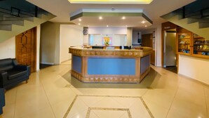 A spacious lobby with a central reception desk, a clock, and a decorative wall. - Kanoa Hotel (Santo Antônio da Platina)
