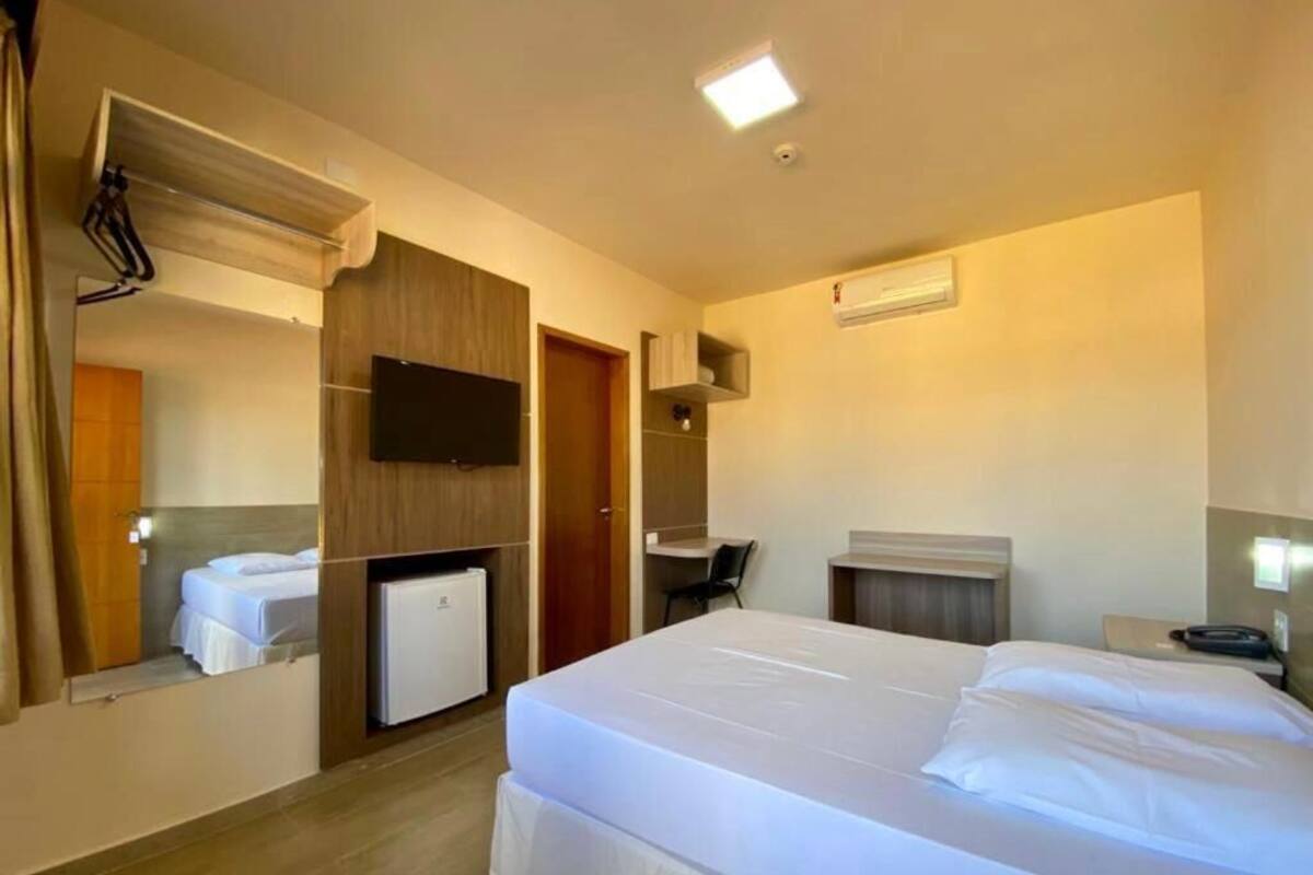 Habitación de hotel con cama, escritorio, silla, refrigerador pequeño y televisor en la pared.